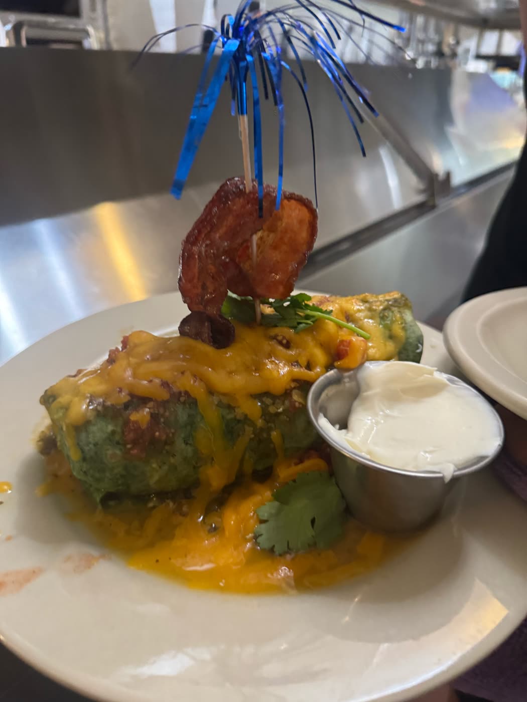 Spinach tortilla burrito smothered in cheddar and topped with bacon, with sour cream