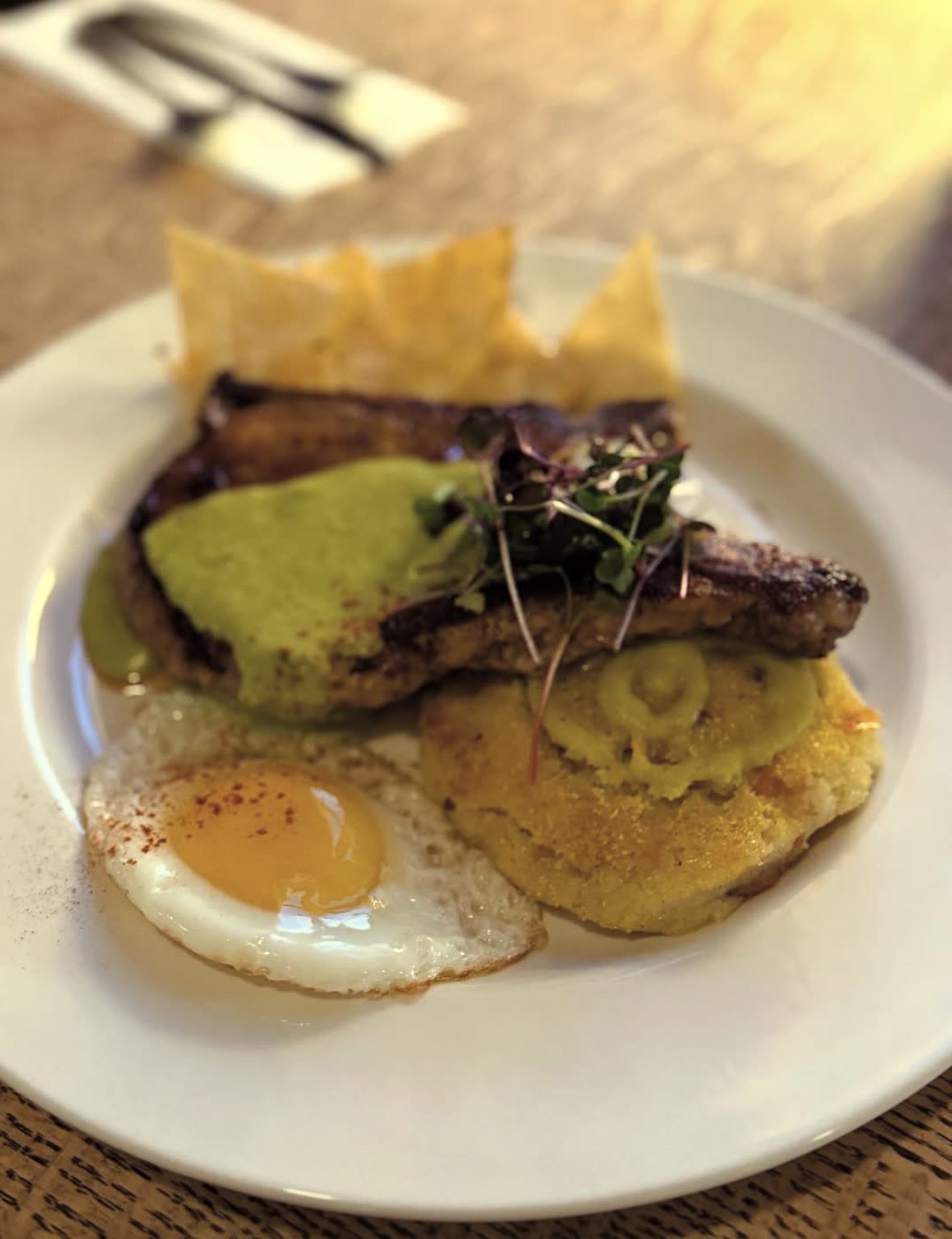Pork chop with green sauce, a fried egg, a cornbread cake and tortilla chips